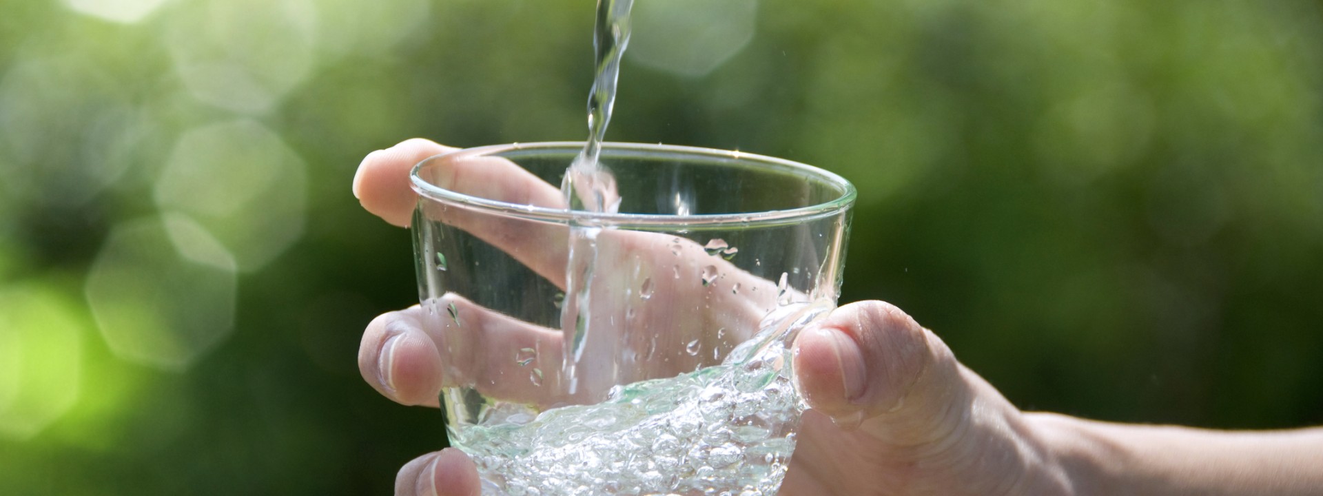 en vandstråle fylder et glas vand der bliver holdt i en hånd