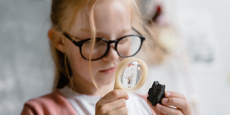 Pige kigger på sten med forstørrelsesglas 