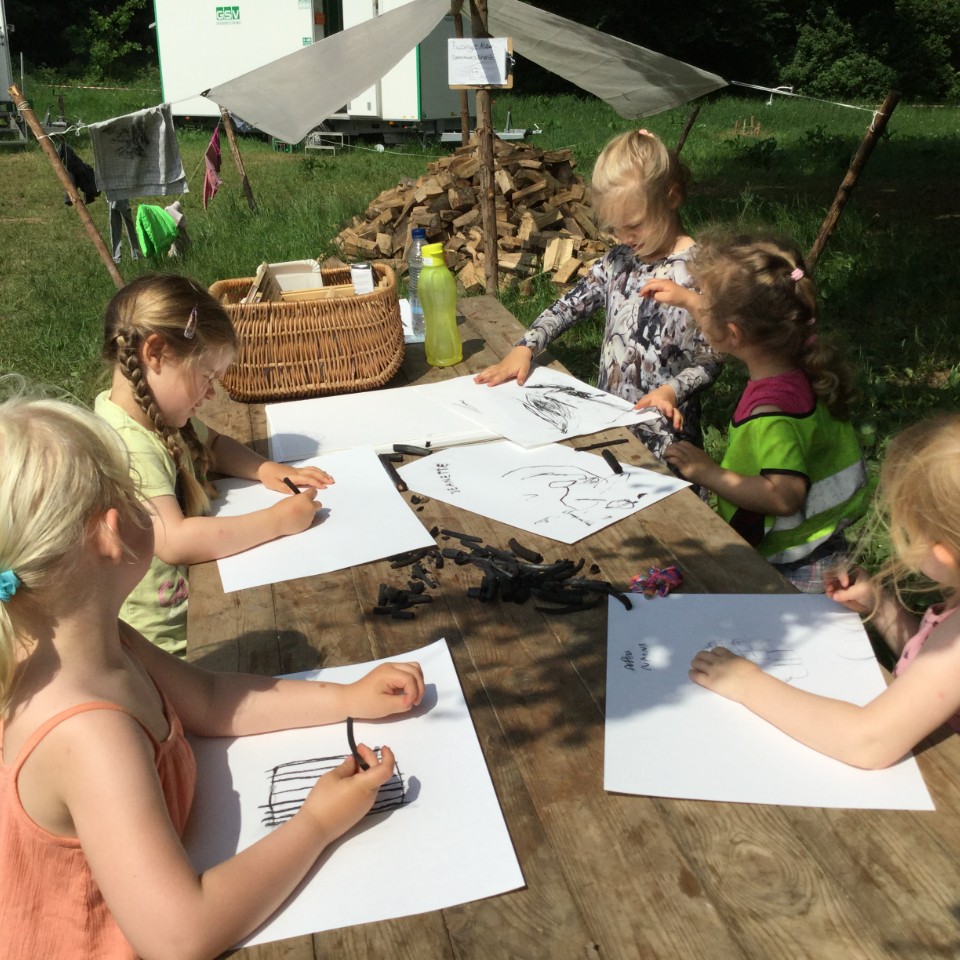 Børn tegner med kul i naturen.