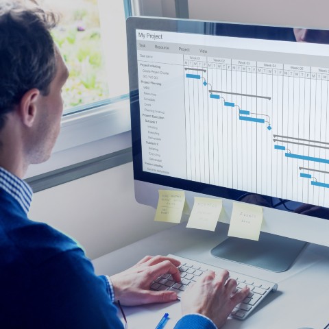 En mand sidder foran en computerskærm med en stor projektplan