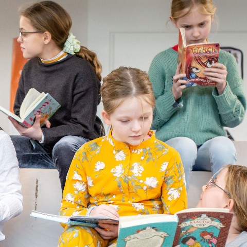 Fire børn læser i bøger på bibliotek
