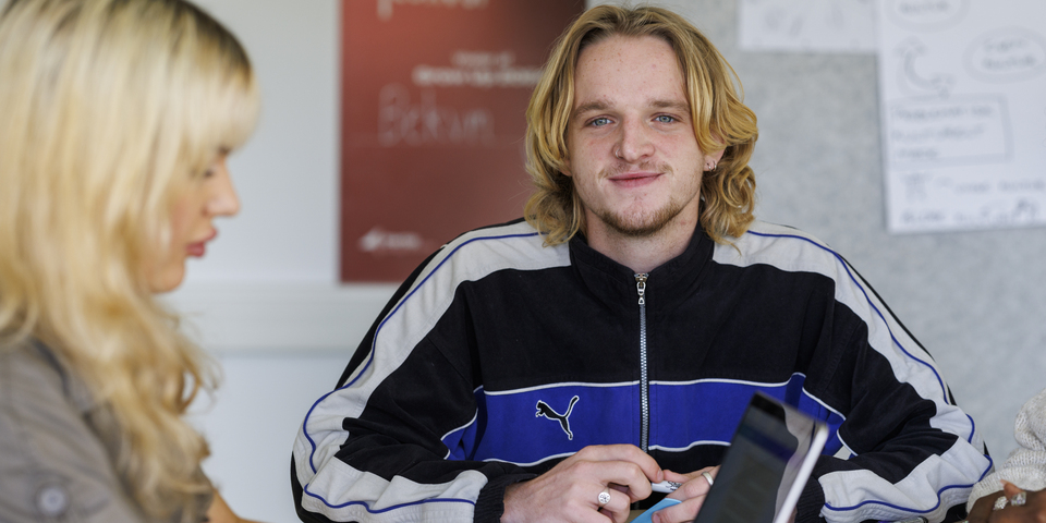 Et gruppearbejde med tre studerende, der noterer på post it's. Computer, bærbar, tusser, grå skjorte, halskæde, træbord, armbånd, fingerringe, diversitet, stemning, tusser, træbord, sorte bænke, noter, bøger, læring, blå, hvid, sort sweatshirt, hårklemme, rød plakat, armbånd. 