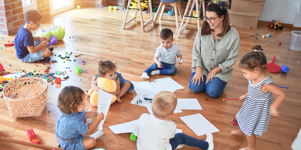 Små børn leger på gulvet i en daginstitution sammen med en pædagog