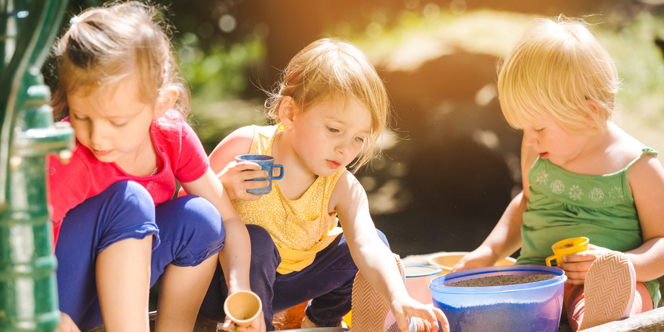 Små børn sidder udendørs i sandkasse og leger mens solen skinner 