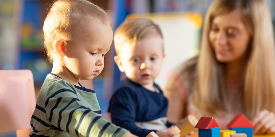 Små børn sidder ved bord og leger med træklodser sammen med pædagog