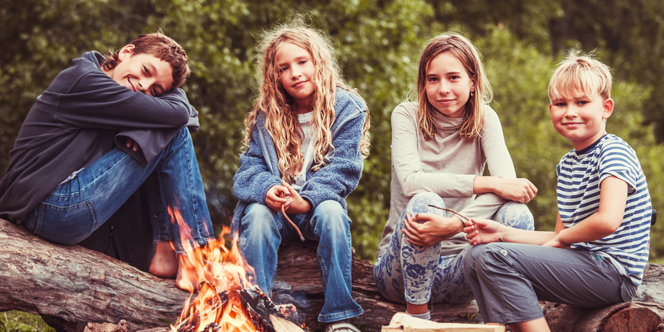 Fire børn sidder omkring et bål og smiler til kameraet 