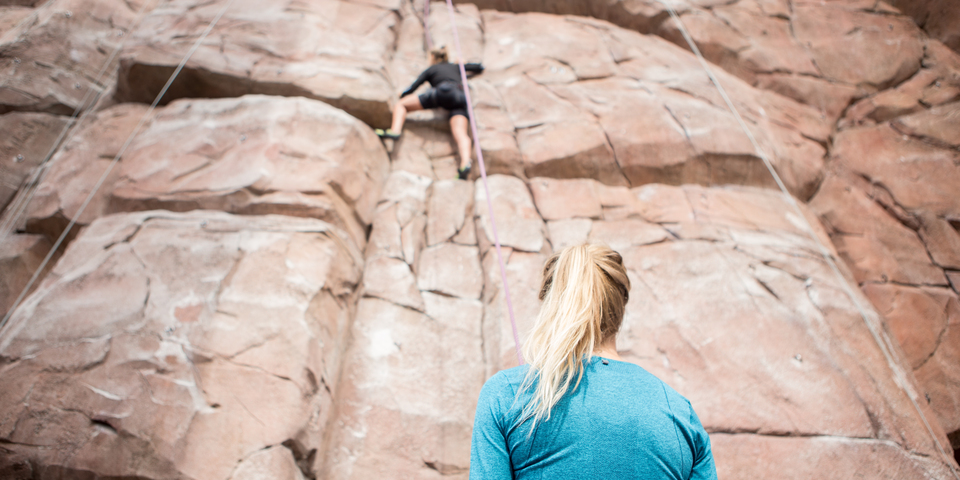 En kvinde klatrer og en anden kvinde kigger på