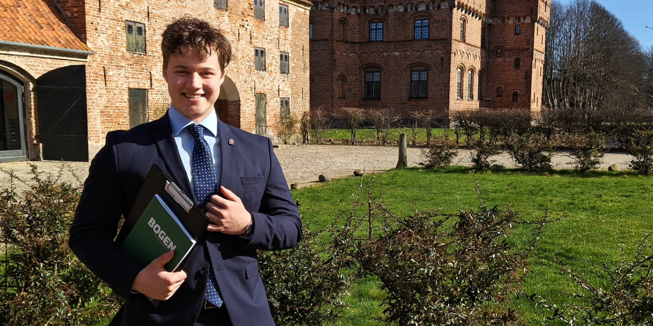 Viktor Thyregod Sivertsen står foran en bygning i jakkesæt med skatterelaterede bøger i hånanden. 