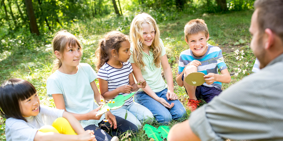 En gruppe børn sidder i en skov sammen med en voksen og laver kreative aktiviteter med blade og planter