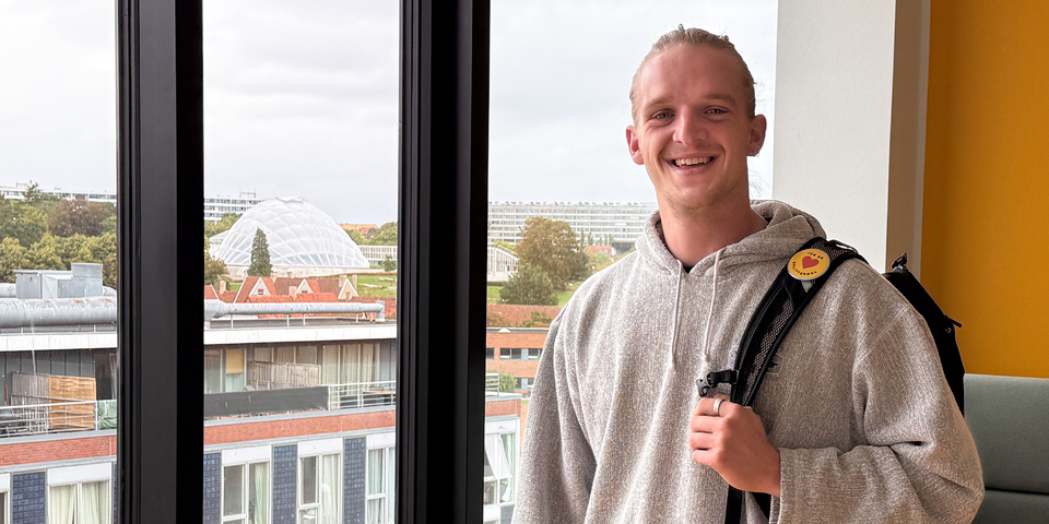 Adam fra civilsamfundsudvikling står ved vindue på Campus Aarhus C med udsigt over Botanisk have og bygninger