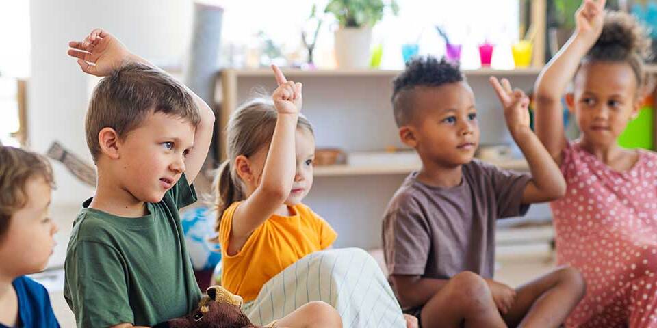Fem børn sidder i en skoleklasse og rækker hånden op
